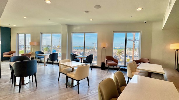 A spacious dining area with multiple tables and chairs, large windows offering a view of the cityscape, and modern lighting fixtures. - Hotel Lydia (Port Aransas)