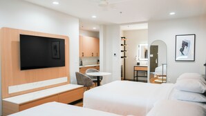 A hotel room with a bed, a TV mounted on the wall, a small table, and a seating area with a bench. - Hotel Lydia (Port Aransas)