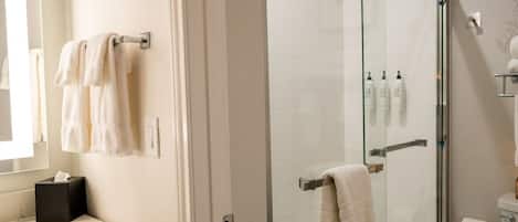 A modern bathroom with a glass shower enclosure, a toilet, and a sink area with towels.