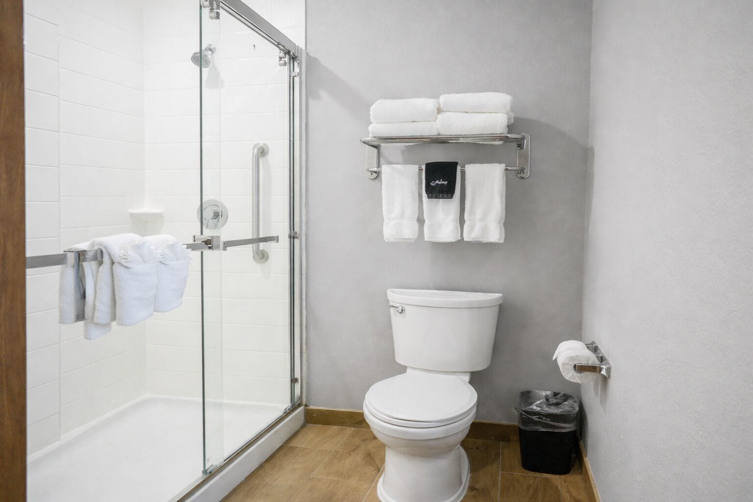 A bathroom with a glass shower enclosure, a toilet, and a towel rack with folded towels.