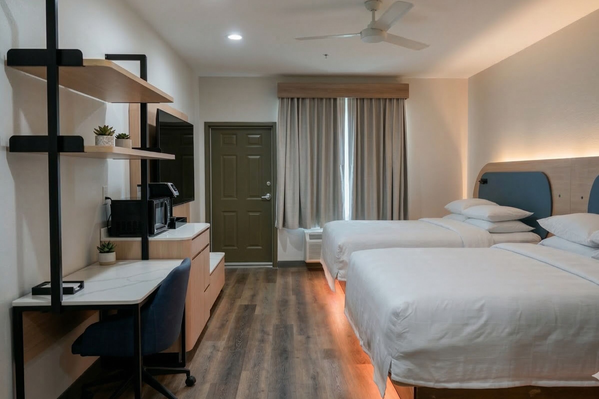 Una habitación de hotel con escritorio, dos camas, armario y ventilador de techo.
