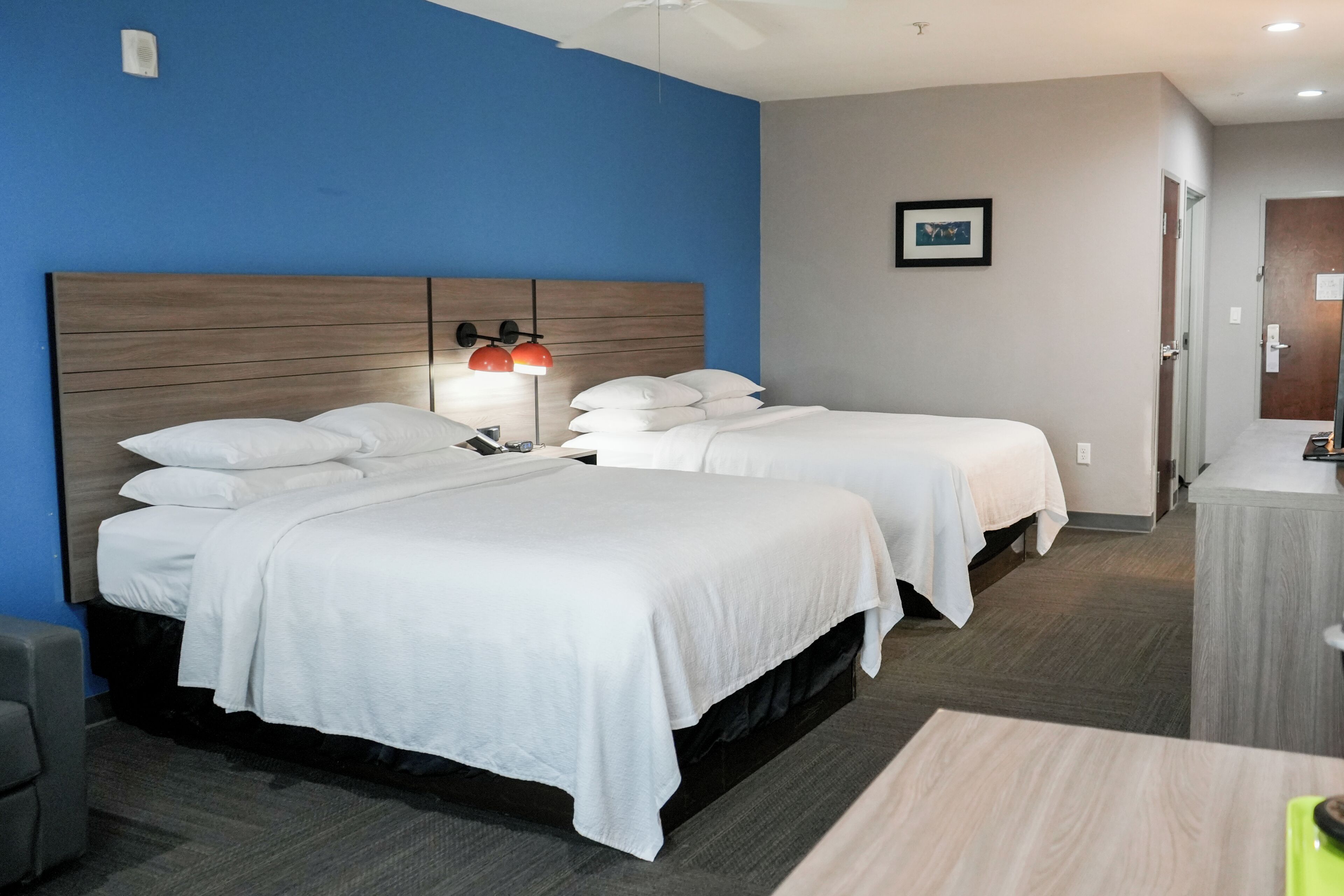 A hotel room with two beds, a desk, a chair, and a ceiling fan.