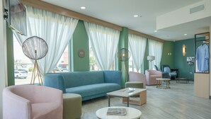 A hotel lobby with a blue sofa, pink chairs, a round table, and a standing floor lamp. - Hotel Lydia (Port Aransas)
