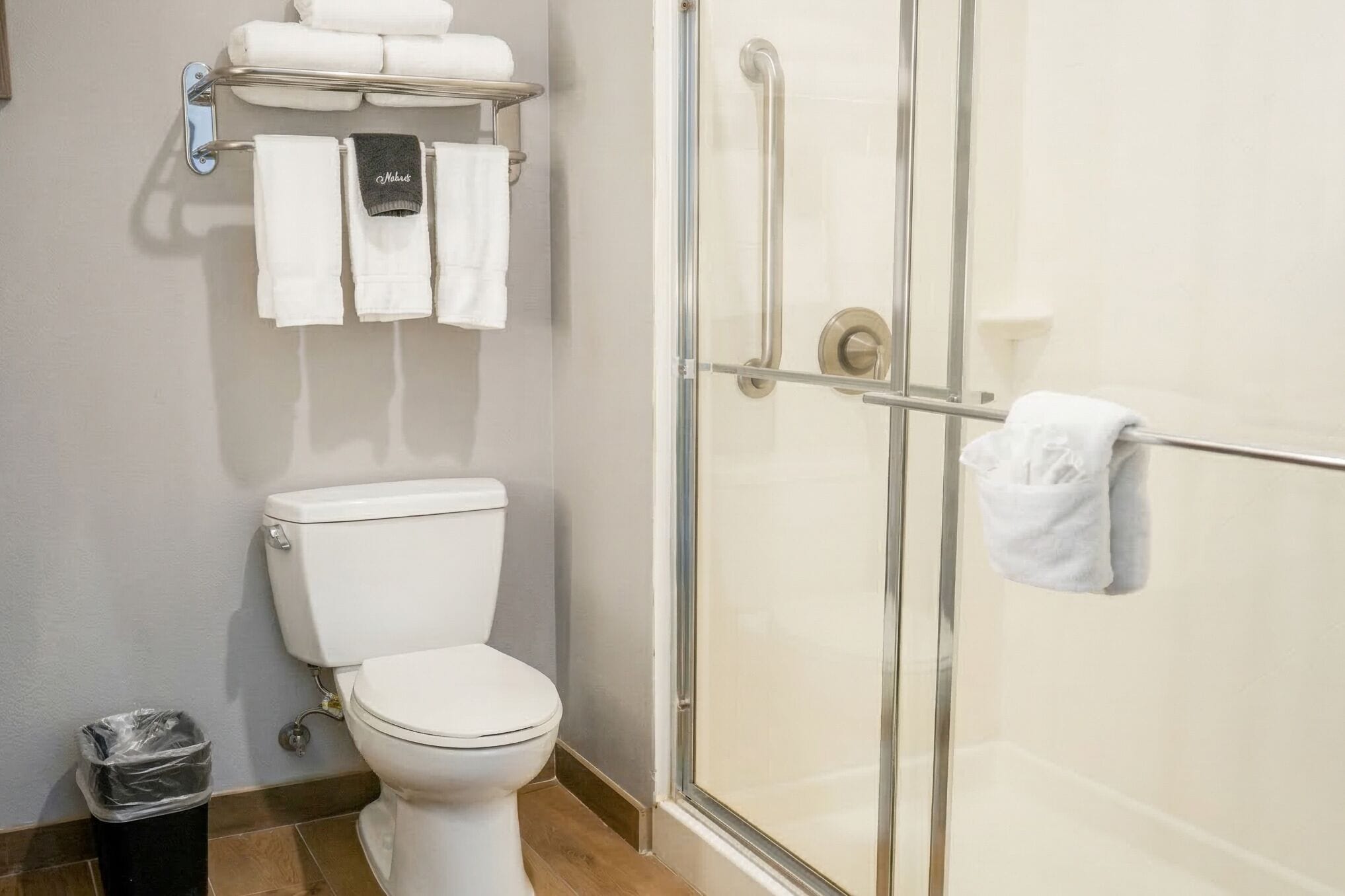 Une salle de bain comprenant des toilettes, une douche fermée par une paroi de verre et un porte-serviettes avec des serviettes.