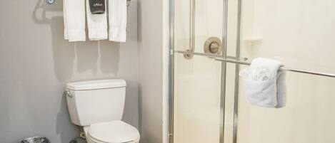 Une salle de bain comprenant des toilettes, une douche fermée par une paroi de verre et un porte-serviettes avec des serviettes.