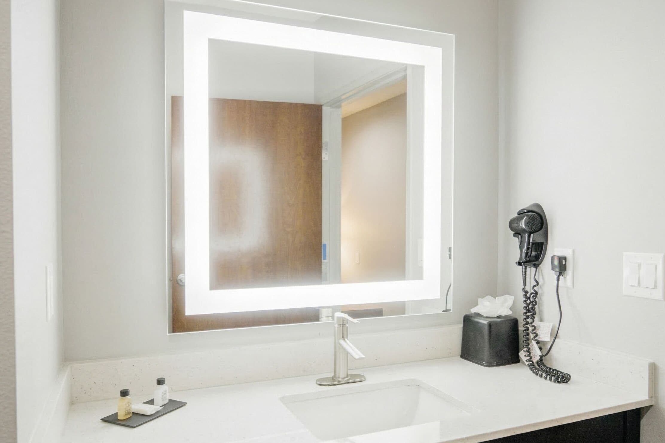 A bathroom with a white sink, a mirror with a light, and a hairdryer on the counter.