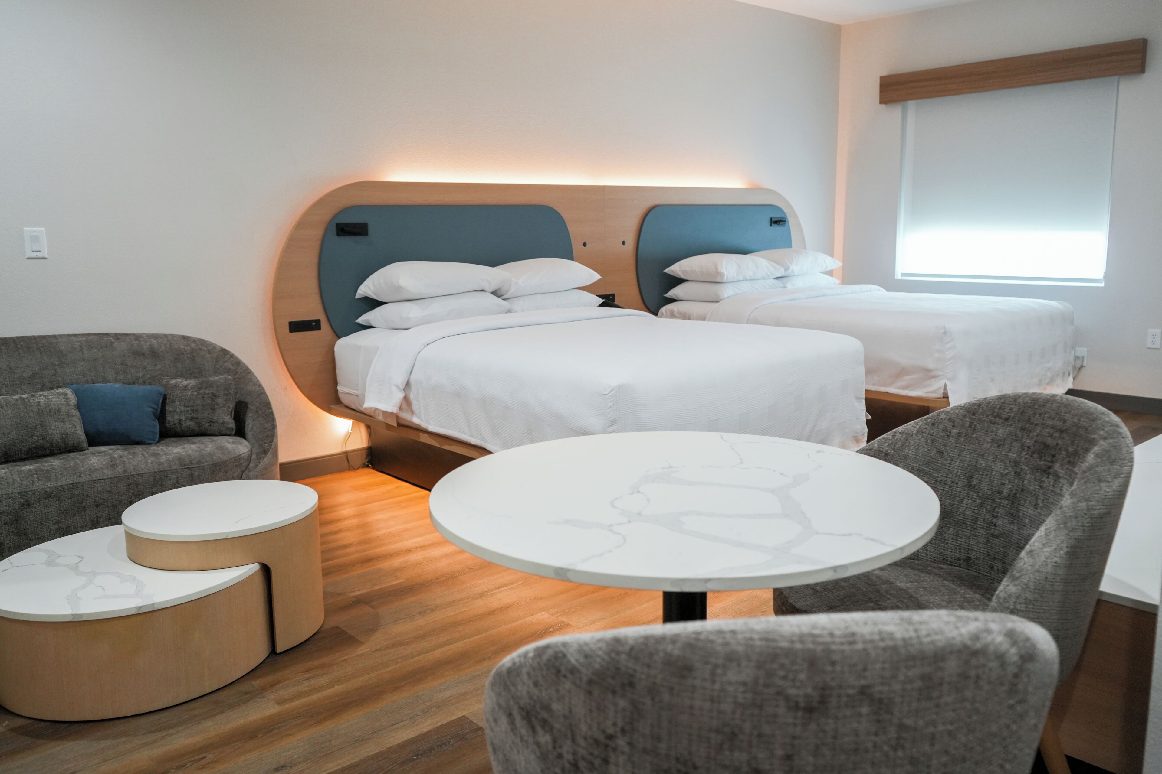 A hotel room with two beds, a sofa, a round table, and a small round table.