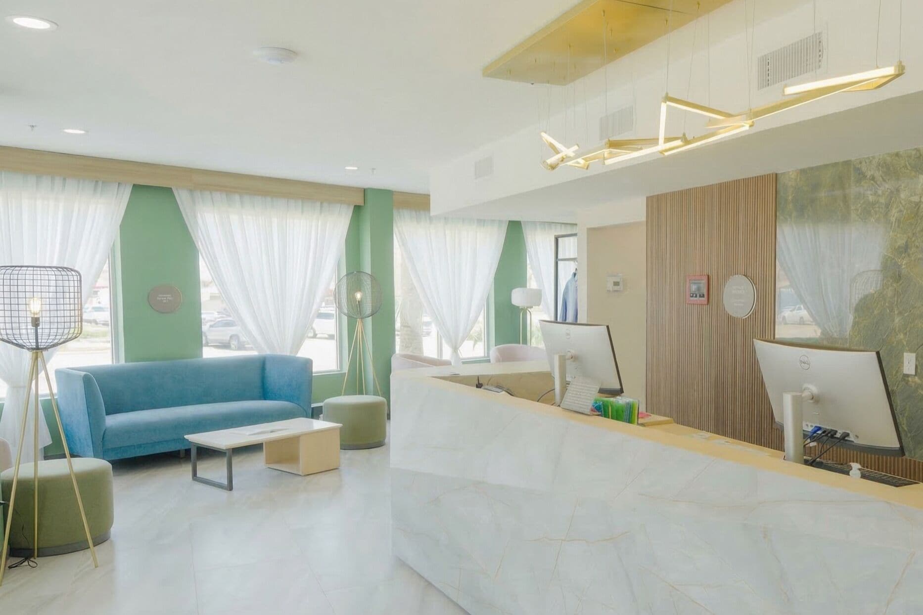 A modern reception area with a blue sofa, a white reception desk, and a large window with sheer curtains.
