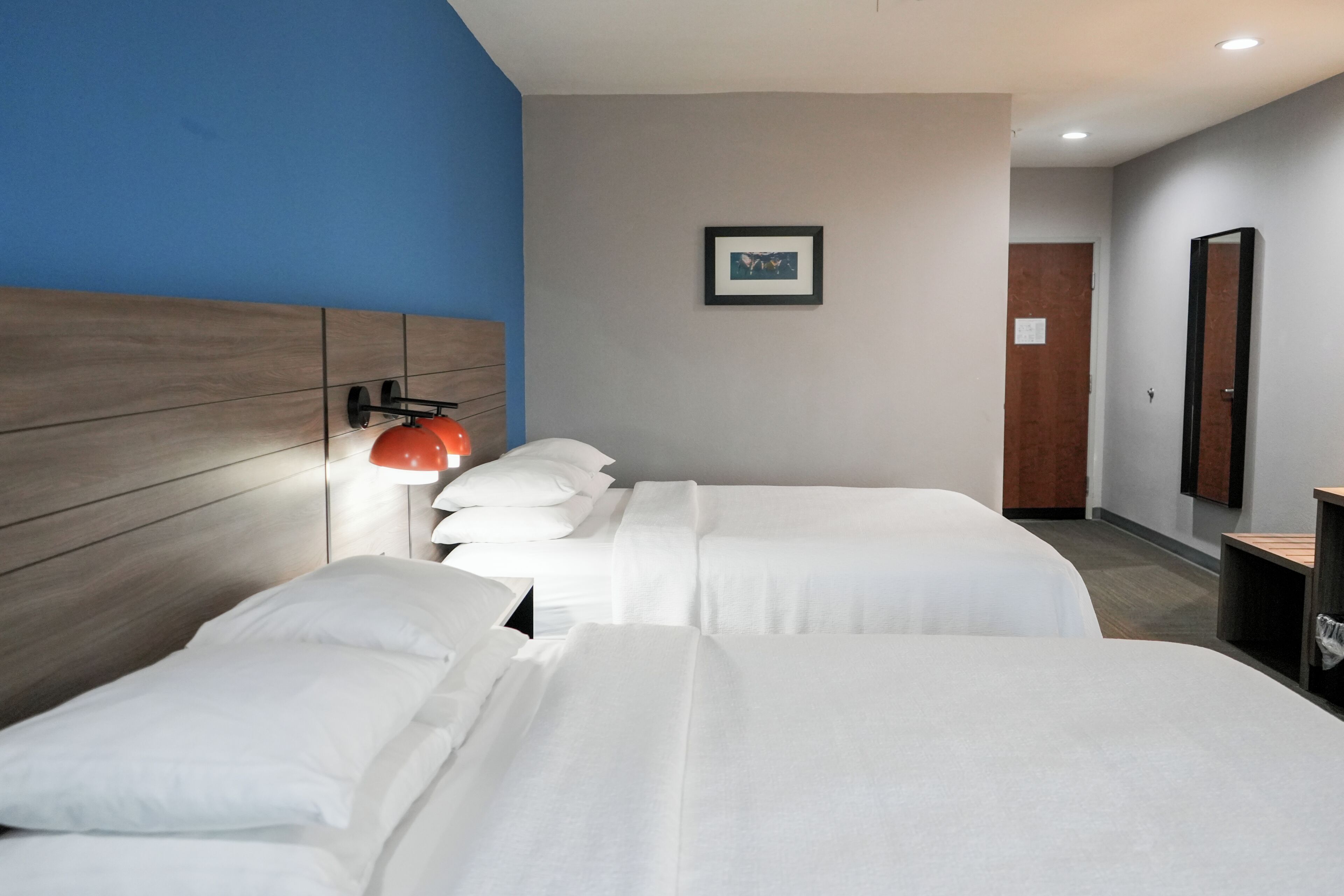 Una habitación de hotel con dos camas, una lámpara roja, un cuadro en la pared y un cabecero de madera.
