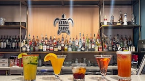 A bar area with a variety of liquor bottles and three different cocktails on the counter. - Hotel Lydia (Port Aransas)