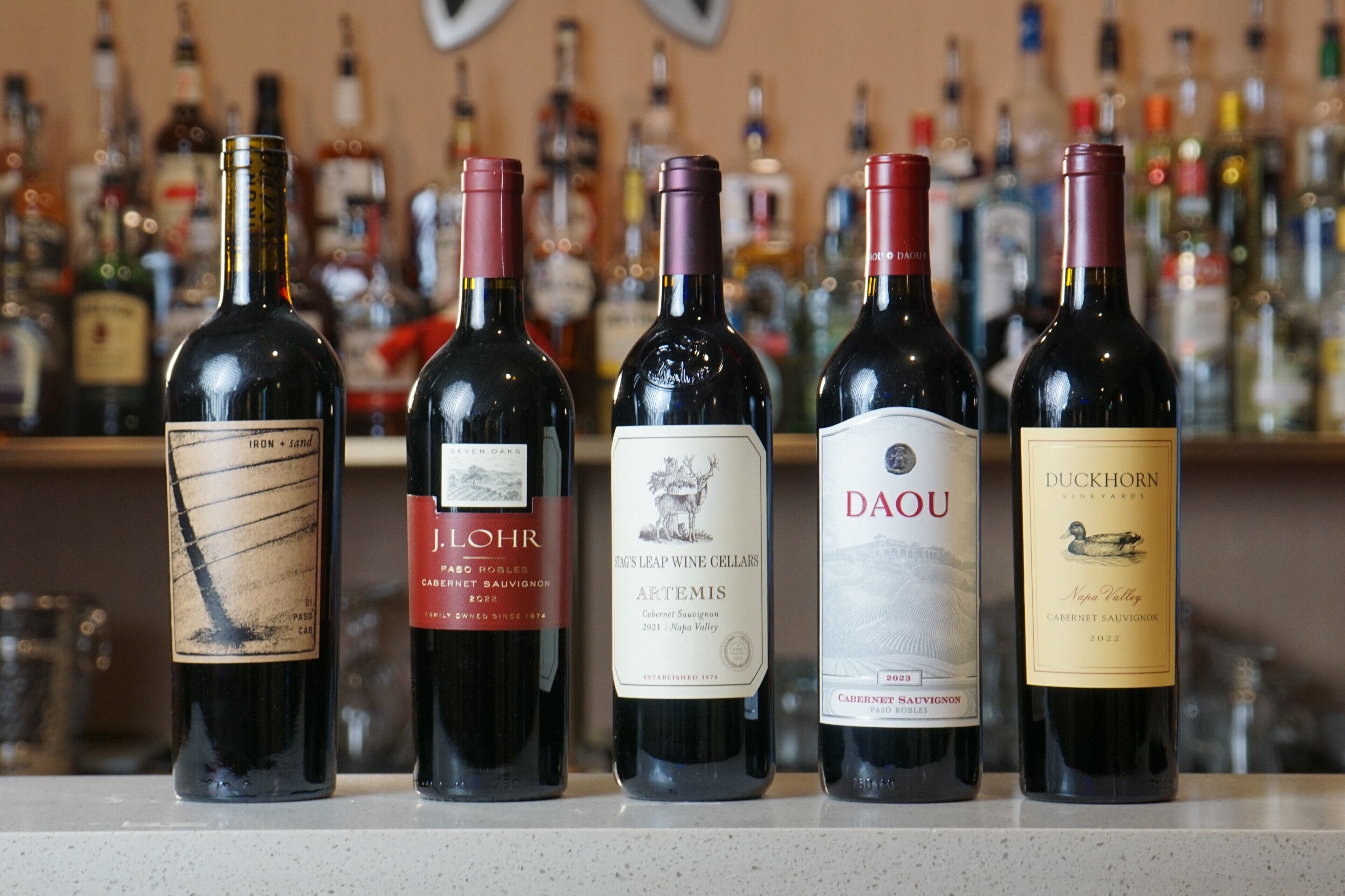 A selection of wine bottles on a bar counter with a blurred background of various bottles.