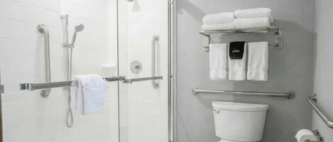 A modern bathroom with a glass shower enclosure, a white toilet, and a towel rack with folded towels.