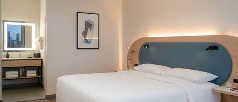Een moderne hotelkamer met een groot bed, een nachtkastje, een spiegel en een lijst met een afbeelding aan de muur.
