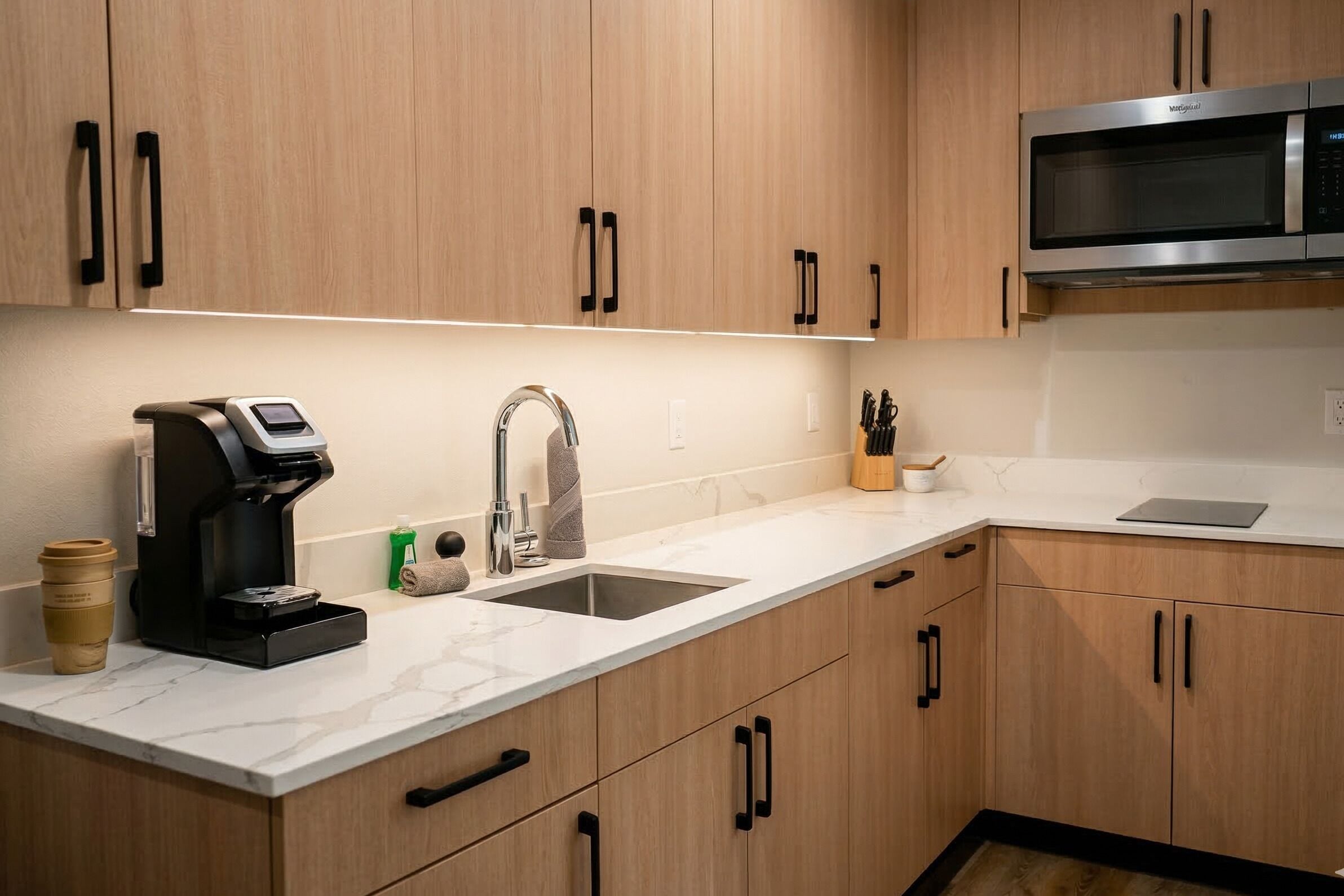 A modern kitchen with wooden cabinets, a stainless steel microwave, a coffee maker, and a sink.
