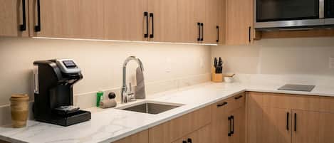 A modern kitchen with wooden cabinets, a stainless steel microwave, a coffee maker, and a sink.