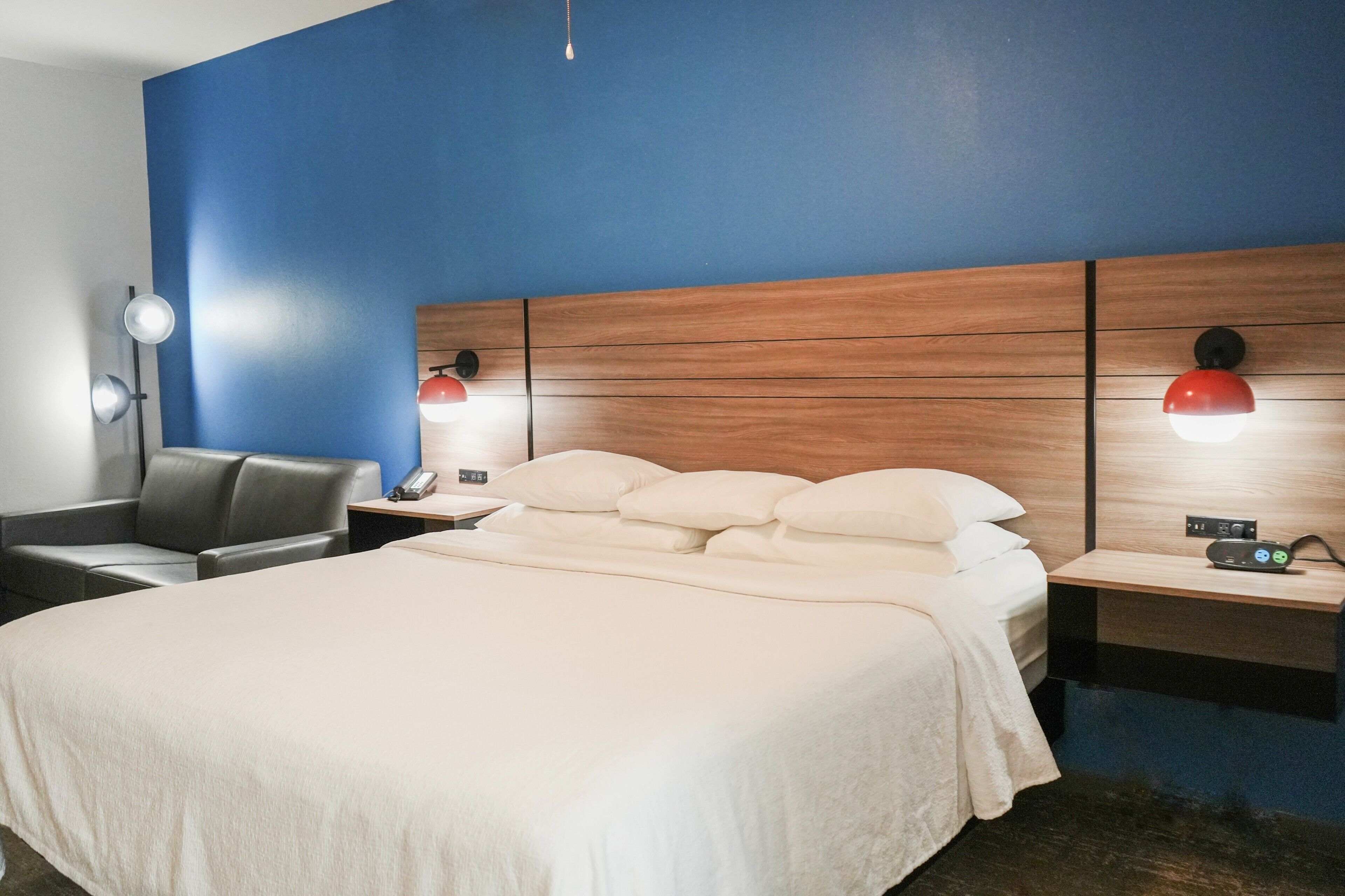 Une chambre d’hôtel avec un grand lit, deux tables de chevet avec des lampes, une chaise et une tête de lit en bois.
