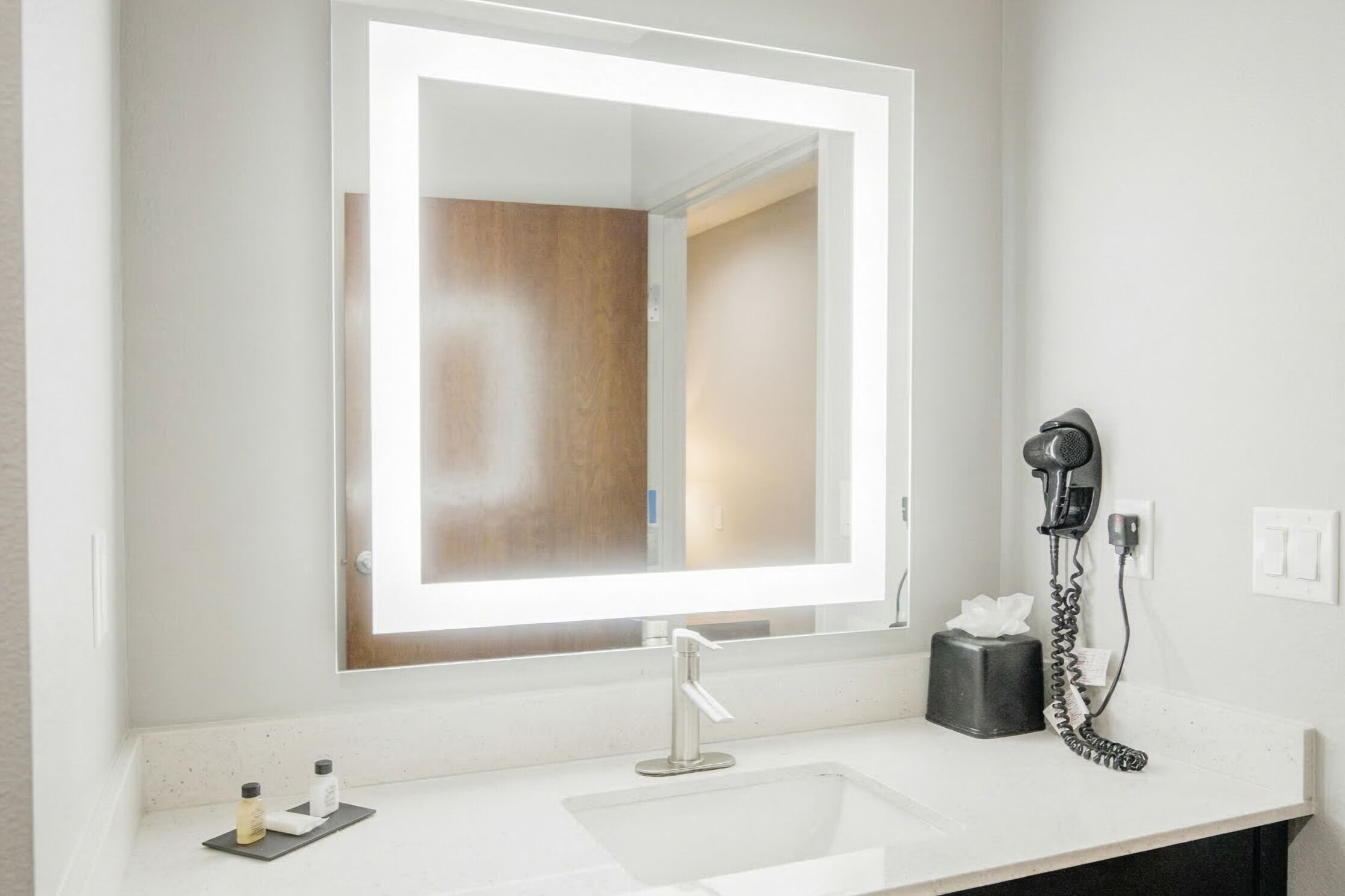 A bathroom with a large mirror, a sink, a hairdryer, and a tissue box.