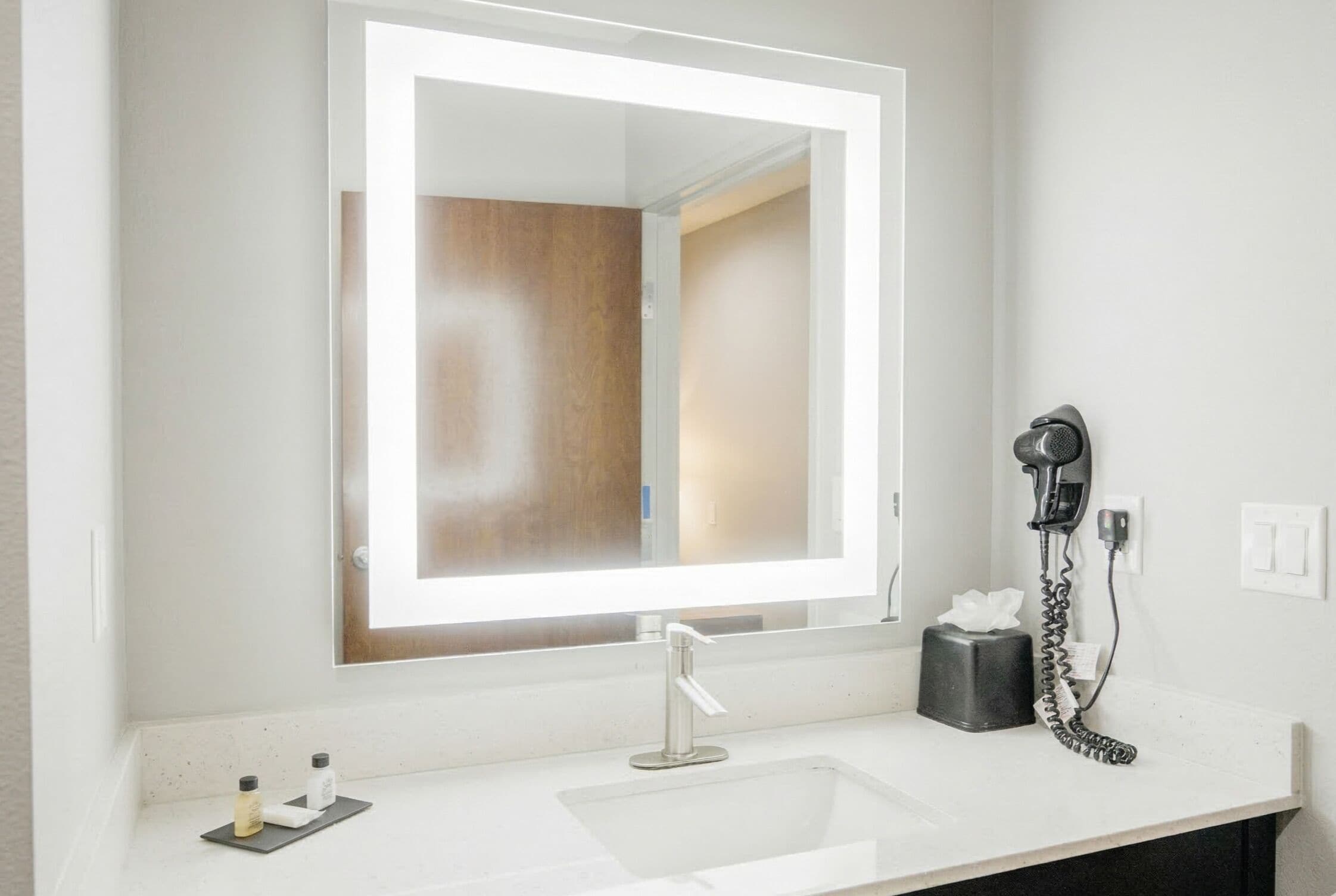 A bathroom with a large mirror, a sink, a hairdryer, and a tissue box.