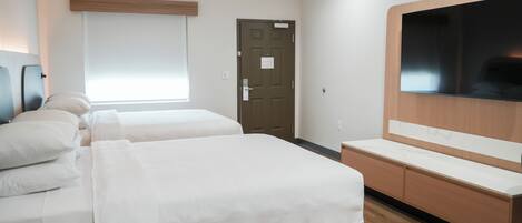 A hotel room with two beds, a TV, a wooden cabinet, and a door.