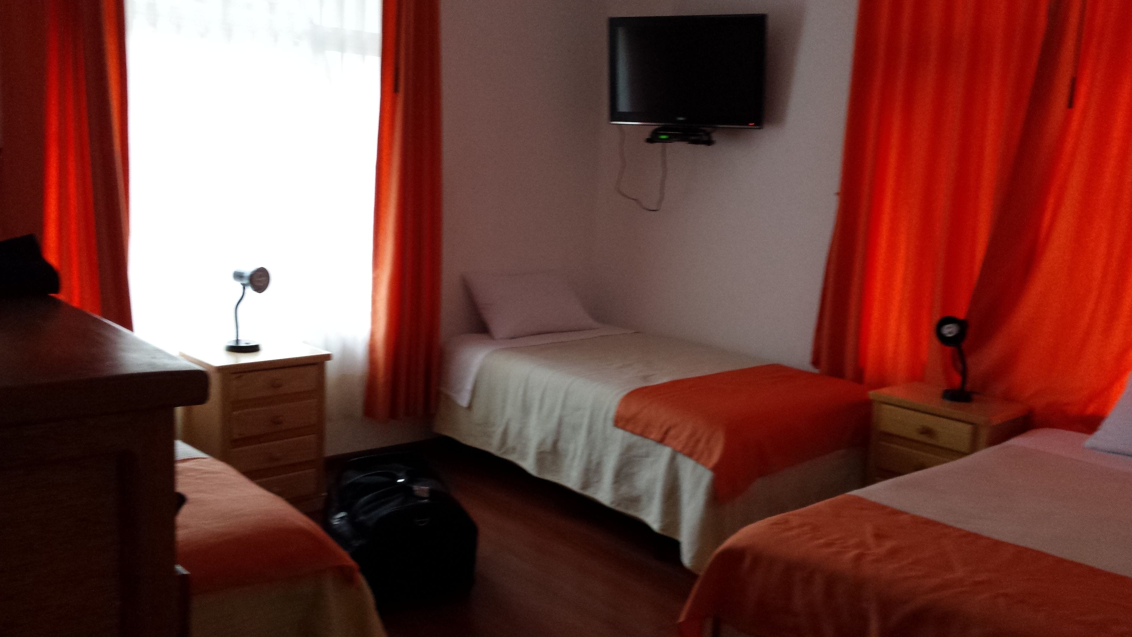 A hotel room with two beds, a TV mounted on the wall, and a desk with a lamp.