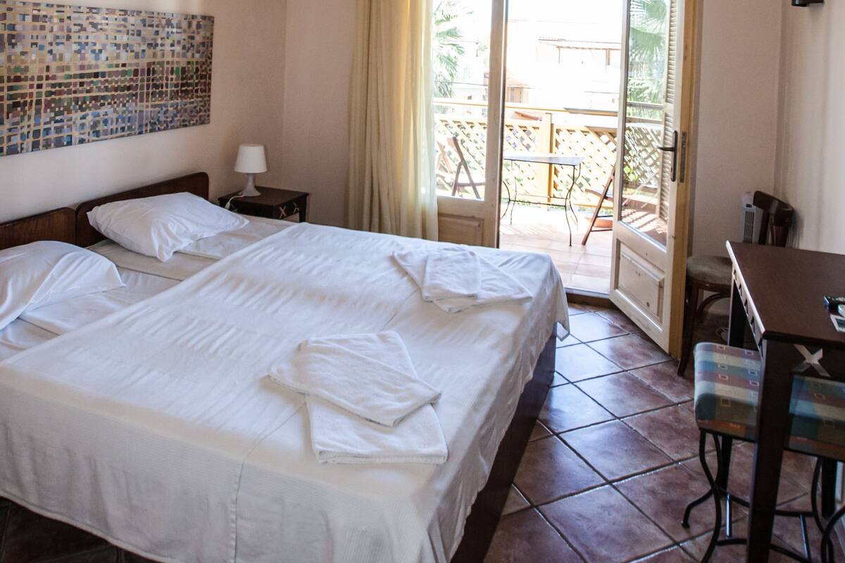 A hotel room with a bed, a desk, a chair, a window with curtains, and a view of the outside.