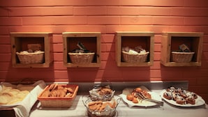A breakfast buffet with various food items displayed in baskets and trays on a table against a brick wall. - Ammon Garden Hotel (Kassandra)