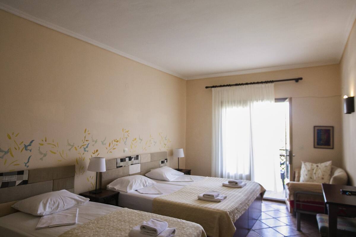 A hotel room with two beds, a chair, a desk, and a window with curtains.