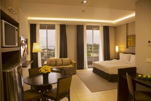 Habitación de hotel con cama, sofá, mesa de comedor con sillas, pequeña cocina y vista al exterior.