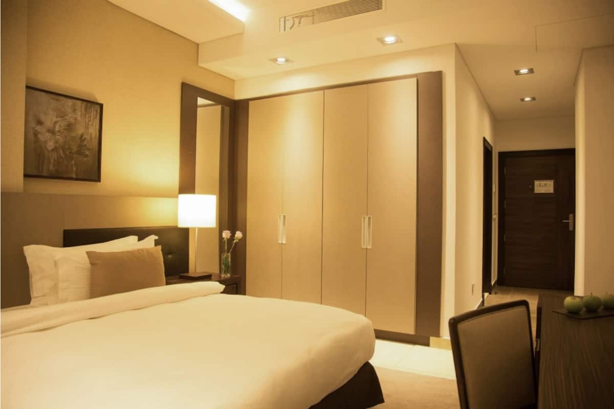 Une chambre d’hôtel avec un grand lit, une table de chevet avec une lampe, un bureau avec une chaise et une armoire.