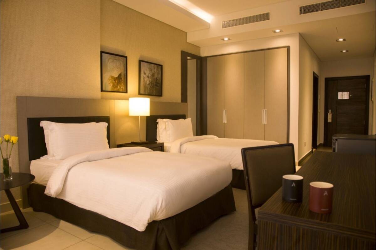 Une chambre d’hôtel avec deux lits, un bureau avec deux tasses, une lampe et un vase avec des fleurs.