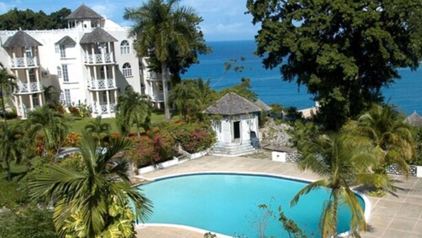 A resort with a large pool, lush greenery, and a view of the ocean.