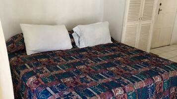 A bedroom with a bed, two pillows, a colorful quilt, a wardrobe, and a painting on the wall.