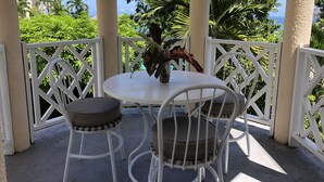 A covered outdoor seating area with a round table and two chairs, surrounded by white lattice railings.