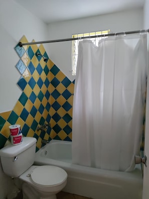 Un baño con inodoro blanco, bañera y cortina de ducha.