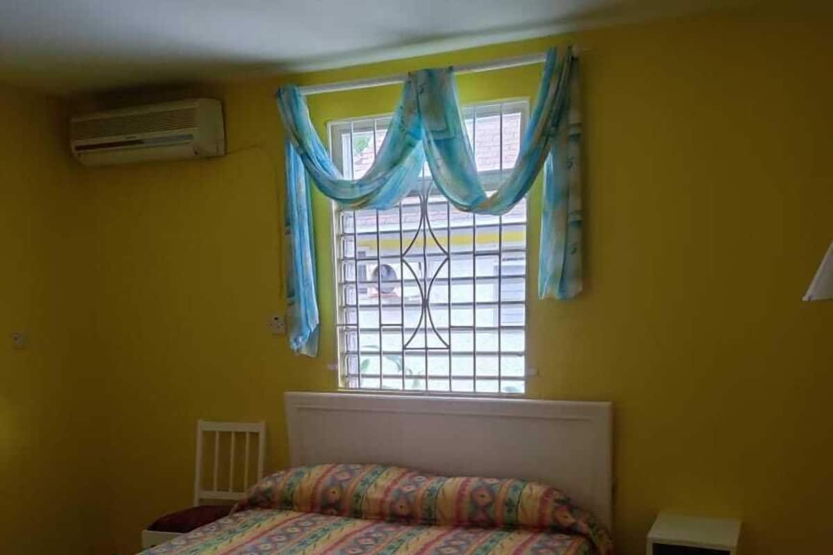 A bedroom with a bed, a window with curtains, a radiator, and a small bedside table.