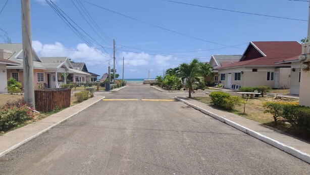 A residential street with houses on both sides, a clear sky, and a view of the ocean in the distance.