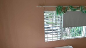 A white sofa with colorful cushions in a room with peach walls, a window with metal bars, and a green curtain.