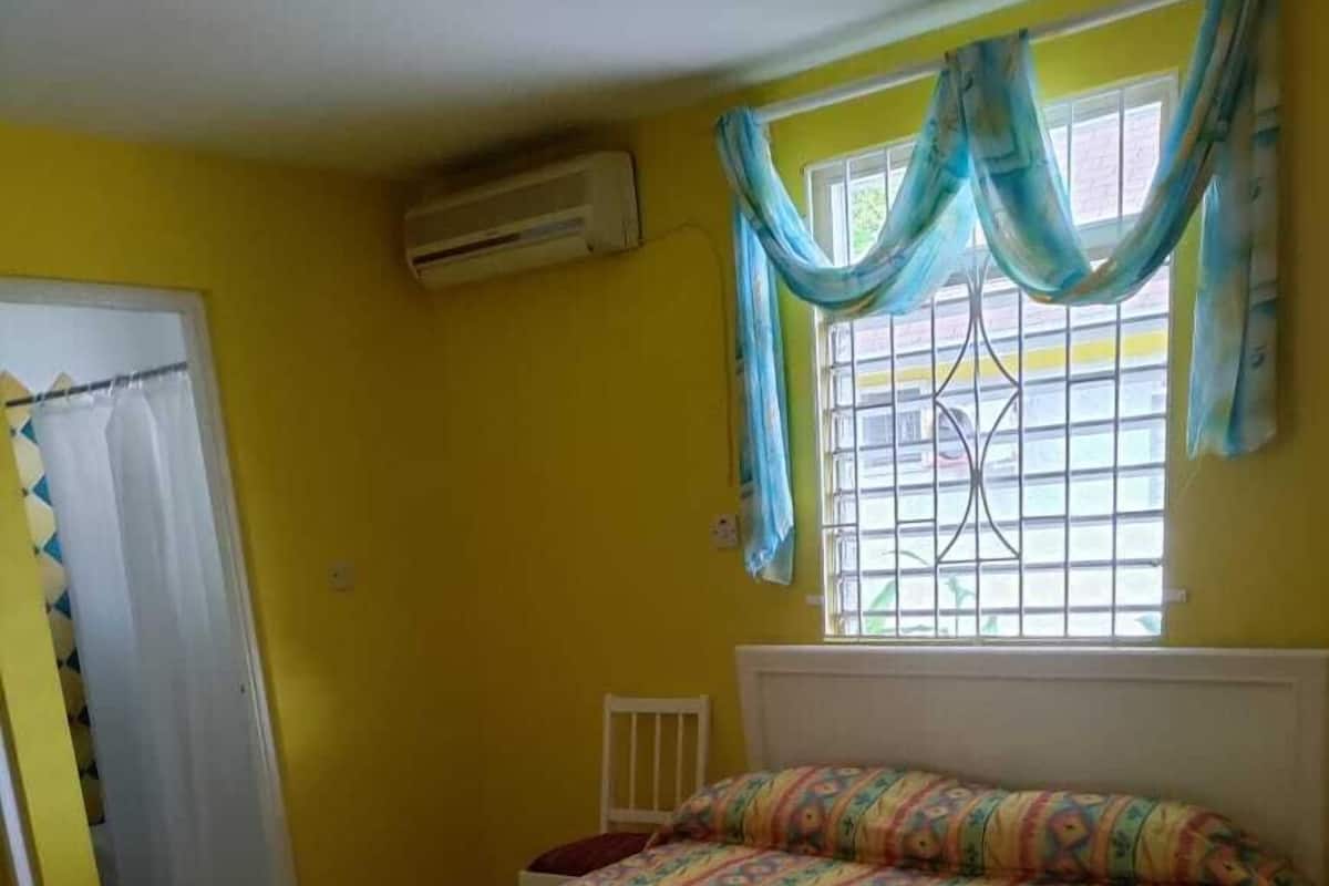 A room with a bed, a window with curtains, and an air conditioning unit.