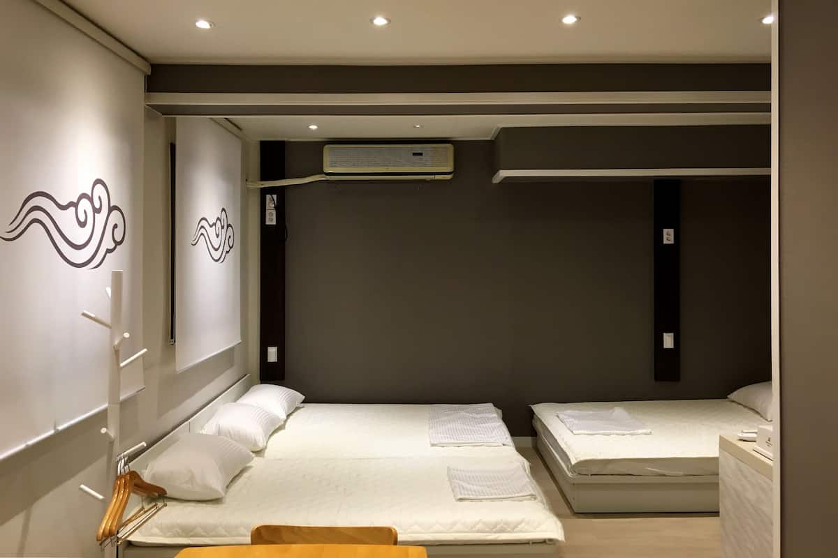 Une chambre d’hôtel avec deux lits, une armoire, un miroir et un climatiseur fixé au mur.