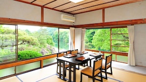 Una habitación japonesa tradicional con suelo de tatami, una mesa de madera con sillas, ventanas grandes con cortinas y un ventilador de techo.