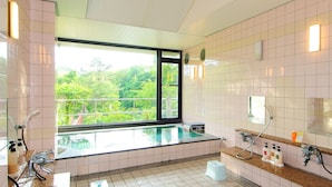 Un baño moderno con un jacuzzi de vidrio, un ventanal con vistas a zonas verdes y un tocador con artículos de aseo.