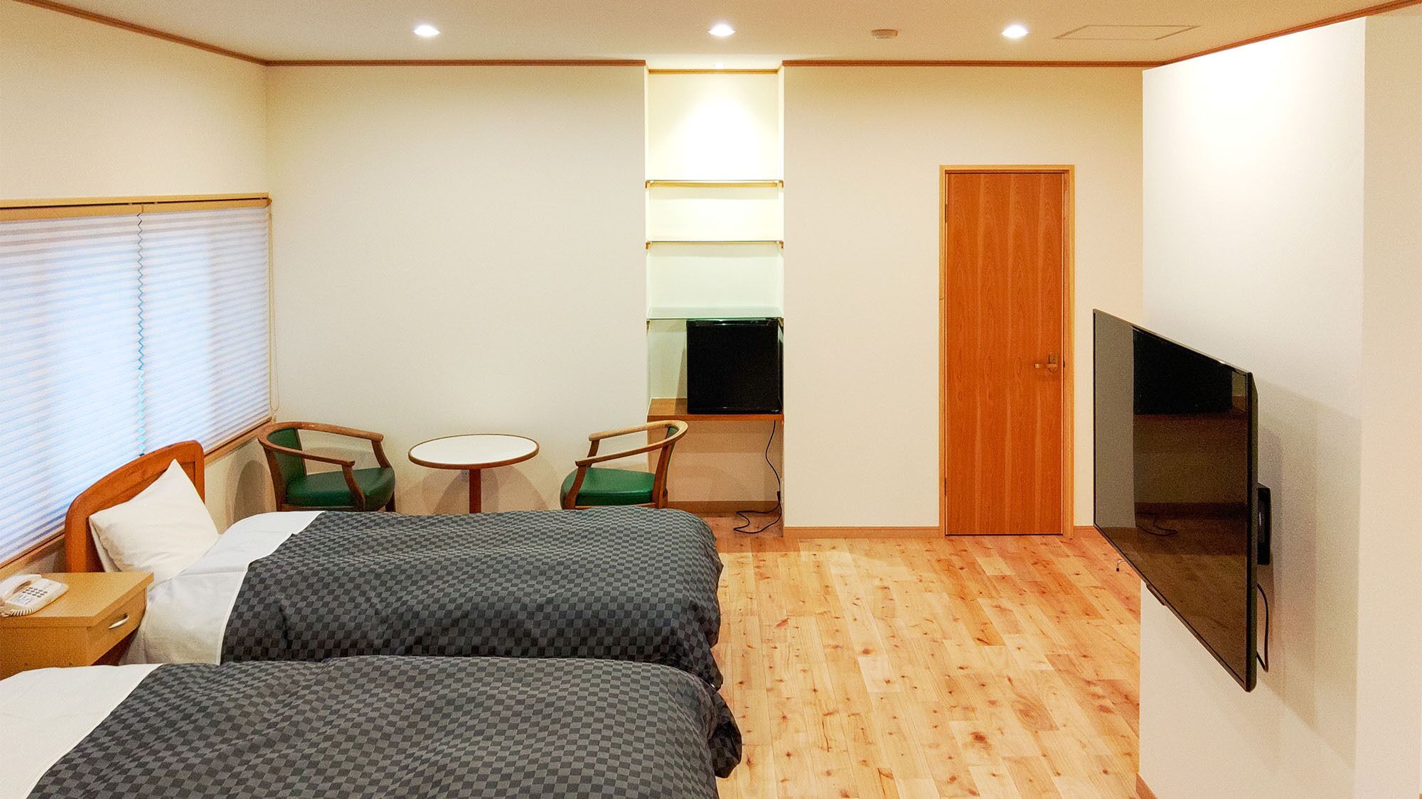 A hotel room with two beds, a TV, a desk with a chair, a small table, and a window with blinds.