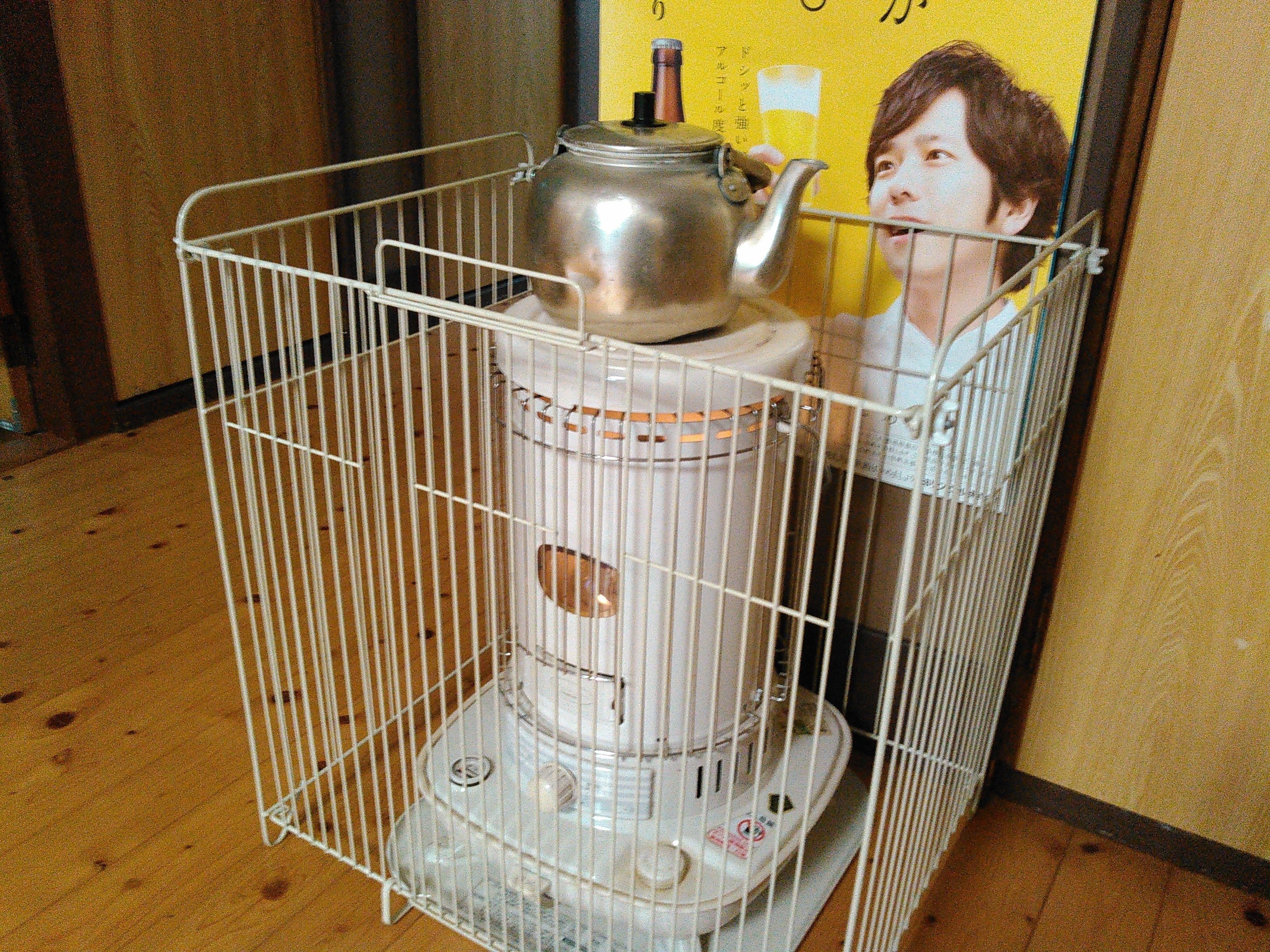 A metal cage with a heating device inside, possibly a stove or heater, placed on a wooden floor.