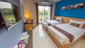 Habitación de hotel con dos camas, un escritorio, una silla, un televisor y un balcón con vistas a zonas verdes.