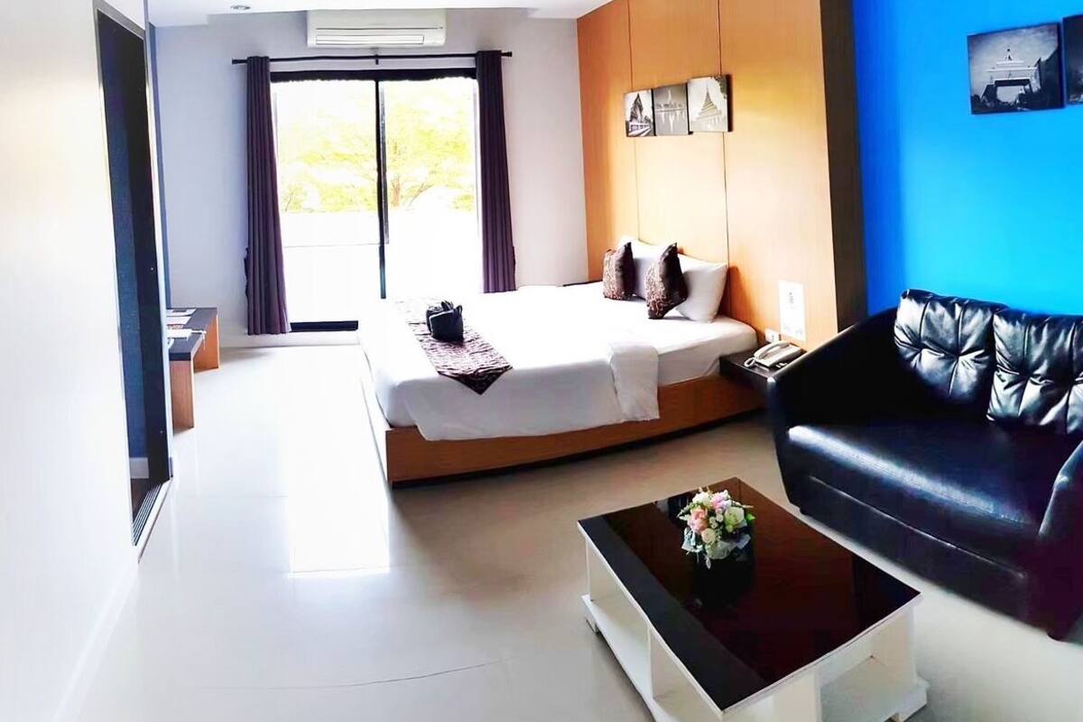 A modern hotel room with a bed, a sofa, a coffee table, and a view of the outdoors.