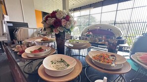 Una mesa de buffet con diversos platos, una parrilla y un jarrón decorativo con flores.