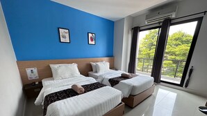 Habitación de hotel con dos camas, una pared de acento azul y un amplio ventanal con vistas a zonas verdes.