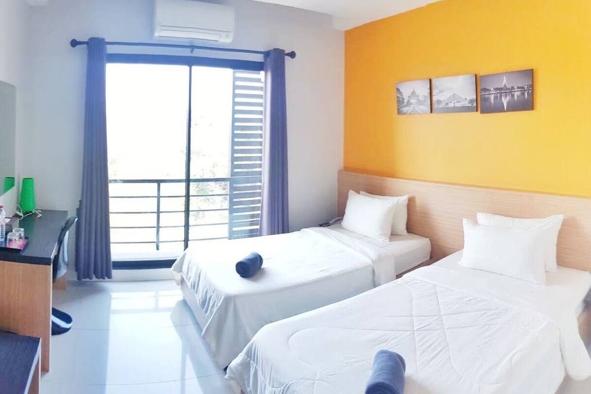 A hotel room with two beds, a desk, and a balcony with curtains.