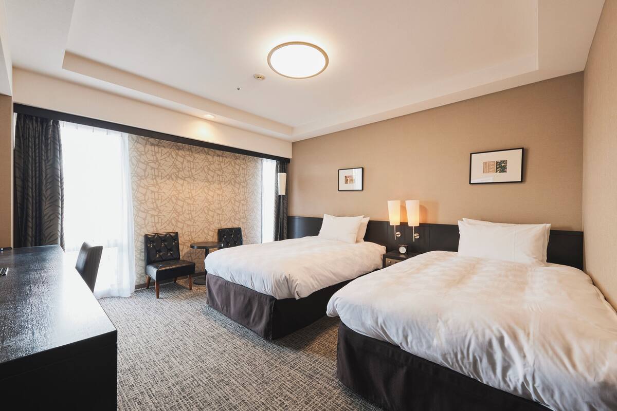 A hotel room with two beds, a desk, and a chair.