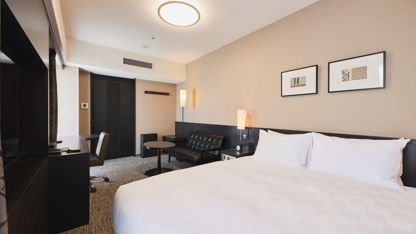 Ein Hotelzimmer mit einem Bett, einem Schreibtisch, einem Sessel, einem kleinen Tisch und zwei gerahmten Bildern an der Wand.